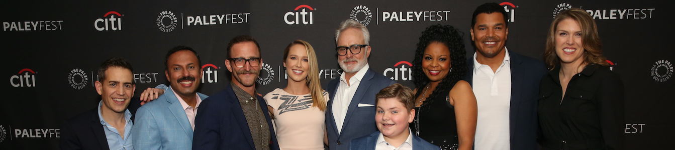 The cast of NBC's Perfect Harmony smiling together in front of logos for Citi and Paleyfest