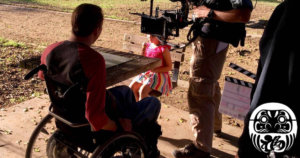Tobias Forest and a young girl on the set of Daruma with a camera pointed at Tobias. Logo for Daruma in bottom right.