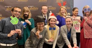 RespectAbility Fall 2018 Fellows with Debbie Fink wearing holiday-related accessories in front of the RespectAbility banner