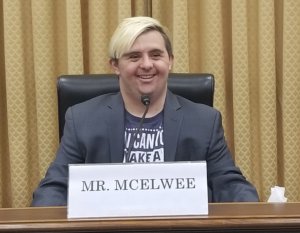 Sean McElwee sits in a hearing room behind a sign that says Mr. McElwee