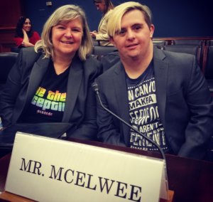 Sandra and Sean McElwee smile together in a Capitol Hill hearing room behind a sign that says Mr. McElwee