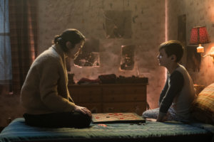A scene from The Parts You Lose with a woman talking to a young boy sitting on a bed. The young boy has a cochlear implant.
