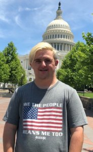 Sean McElwee wearing a shirt that says We The People Means Me Too with an American flag and the Seanese logo on it, standing in front of the Capitol dome.