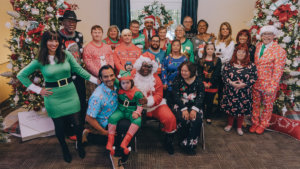 The cast of Born This Way, including their families, smiling together in front of Christmas trees wearing festive clothes