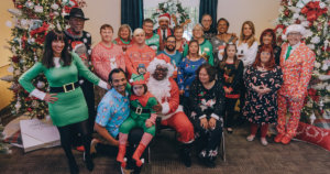 The cast of Born This Way, including their families, smiling together in front of Christmas trees wearing festive clothes