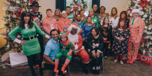 The cast of Born This Way, including their families, smiling together in front of Christmas trees wearing festive clothes