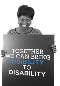 A woman holding a sign that says "Together we can bring Visibility to Disability", smiling