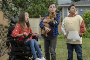 three pre-teens, one girl in a wheelchair, and two boys standing, one holding a dog