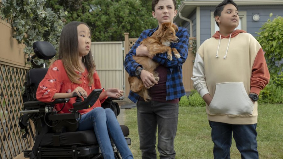 three pre-teens, one girl in a wheelchair, and two boys standing, one holding a dog