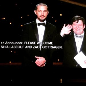 Zack Gottsagen presenting with Shia LeBeouf on stage at the 2020 Academy Awards with captions on screen