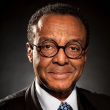 Clarence Page headshot wearing black suit, white shirt and glasses