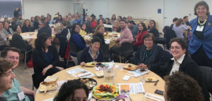 a group picture of people seated at round tables facing the camera smiling