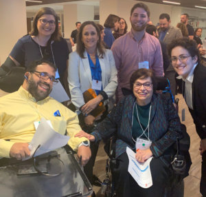 A group of individuals with disabilities, two seated in wheelchairs, smiling for the camera