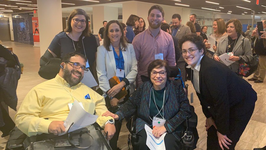 A group of individuals with disabilities, two seated in wheelchairs, smiling for the camera