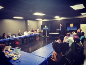 Summer Lab participants seated around a table listening to a lecture