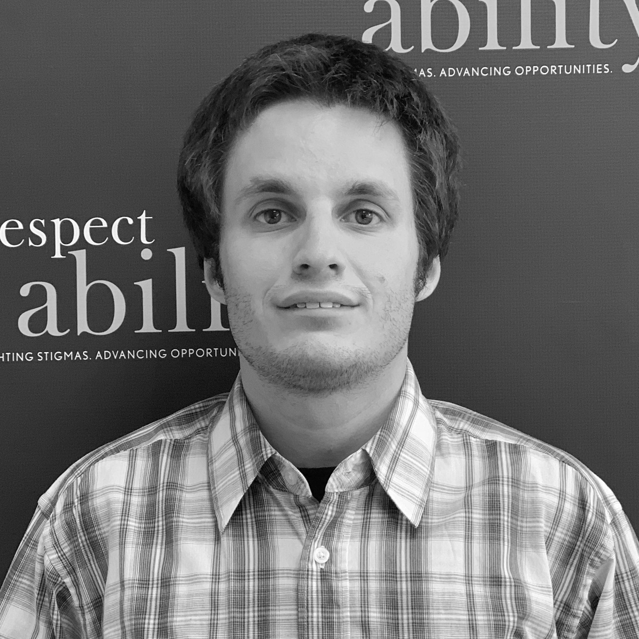 Ilya Zhitomirskiy smiling in front of the RespectAbility banner