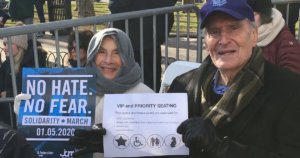 Elderly couple seated at solidarity rally in priority seating section holding signs for the march and the priority seating section
