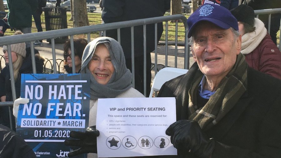 Elderly couple seated at solidarity rally in priority seating section holding signs for the march and the priority seating section