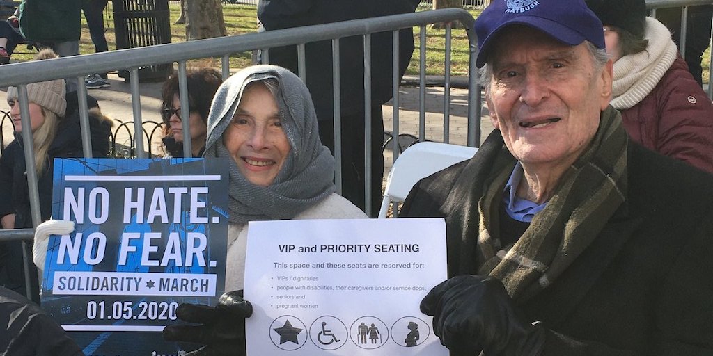 Elderly couple seated at solidarity rally in priority seating section holding signs for the march and the priority seating section