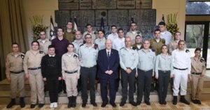 Israeli President Rivlin and Special in Uniform soldiers smile together in front of Israeli flags, standing on steps