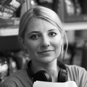 Ashley Eakin with a pair of over-ear headphones around her neck on a film set, smiling