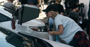 Ashley Eakin on the set of a film shoot looking into a monitor next to two cars