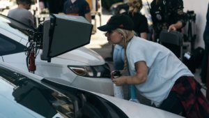 Ashley Eakin on the set of a film shoot looking into a monitor next to two cars