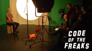 A person with a disability being interviewed for the documentary Code of the Freaks. Logo for the film in bottom right