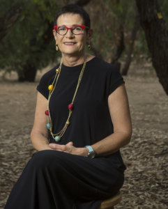 Hilla Hadas smiling headshot seated in front of a tree