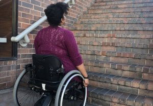 An African American woman in a wheelchair looking up a flight of stairs