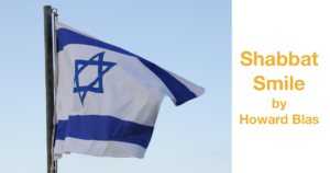 An Israeli flag flying against a blue sky. Text: Shabbat Smile by Howard Blas