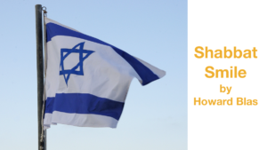 An Israeli flag flying against a blue sky. Text: Shabbat Smile by Howard Blas