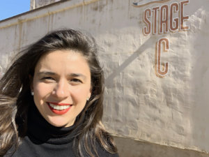 Alexandra Grossi headshot smiling in front of a wall that says Stage C