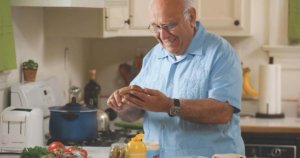 A man in his kitchen holding bread and a knife, making a sandwich.