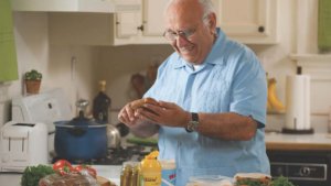 A man in his kitchen holding bread and a knife, making a sandwich.