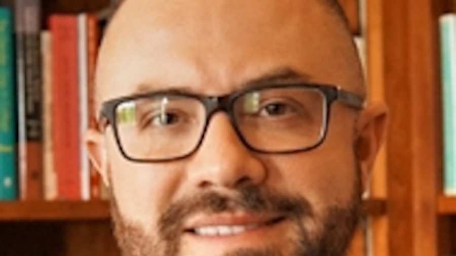 Paul Luelmo headshot smiling. Luelmo has brown hair, a beard and mustache, and glasses