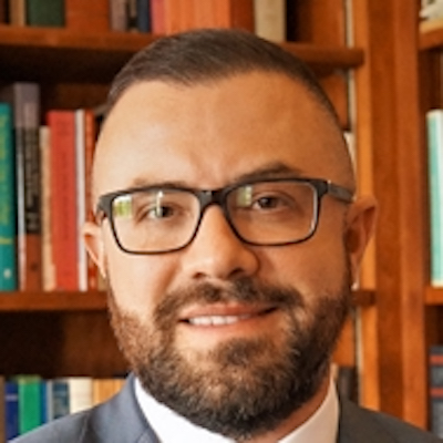 Paul Luelmo headshot smiling. Luelmo has brown hair, a beard and mustache, and glasses