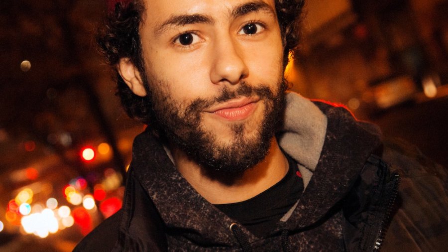 Ramy Youssef headshot wearing a red cap backwards