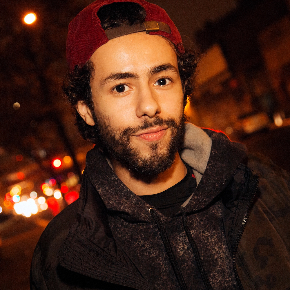 Ramy Youssef headshot wearing a red cap backwards