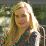 Ariella Barker smiling headshot. Barker is a white woman with blonde hair down past her shoulders who uses a wheelchair