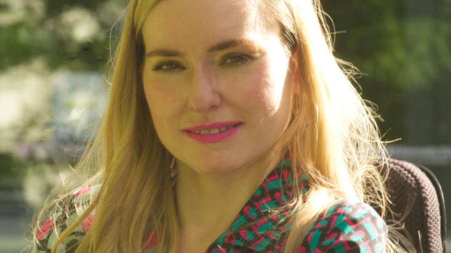 Ariella Barker smiling headshot. Barker is a white woman with blonde hair down past her shoulders who uses a wheelchair