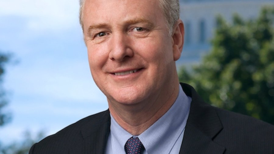 Chris Van Hollen smiling wearing a suit and tie with the US Capitol dome in the background behind him.