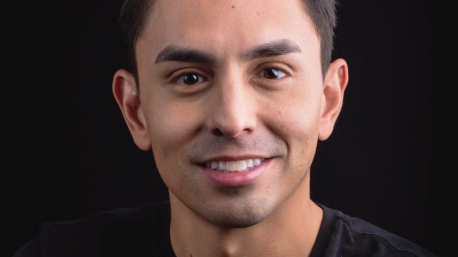 Danny Gomez smiling headshot wearing a black shirt in front of a black backdrop