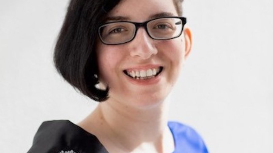 Lauren Arena headshot smiling wearing a sash that says Ms. Wheelchair New York on it. Arena is a white woman with black hair down one side of her head