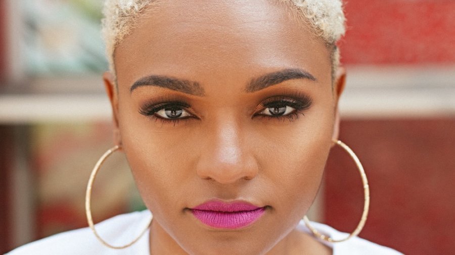 Lolo Spencer smiling headshot. Lolo is a woman of color with short hair and hoop earrings