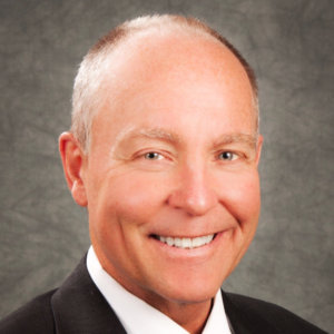 Mark Allan Schultz smiling wearing a suit. Schultz is a white man with very short hair