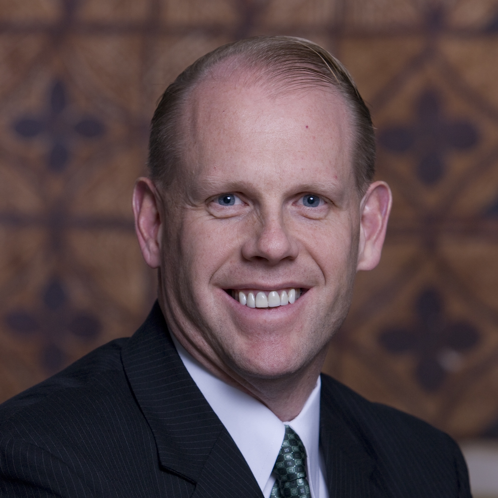 Mark Feinour smiling wearing a suit and tie. Mark is a white man with short brown hair.