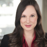 Rachel Handler smiling headshot. Rachel is a white woman with brown hair down to her shoulders, and is wearing a black jacket and red shirt