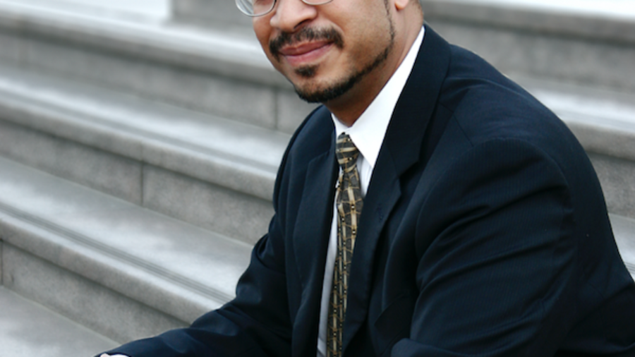 Stephen David Simon sitting on a stone staircase wearing a suit and tie and glasses.