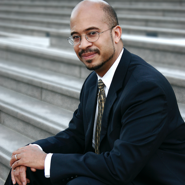 Stephen David Simon sitting on a stone staircase wearing a suit and tie and glasses.
